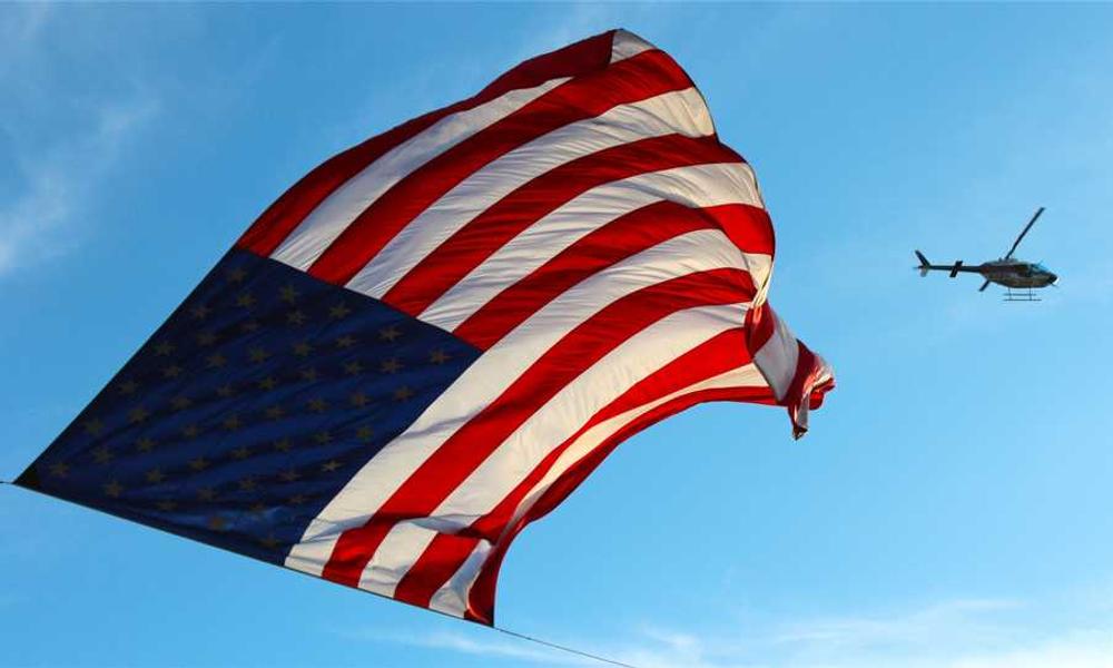 Amerikanische Flagge im Wind mit Hubschrauber, symbolisiert Freiheit - RentPilot