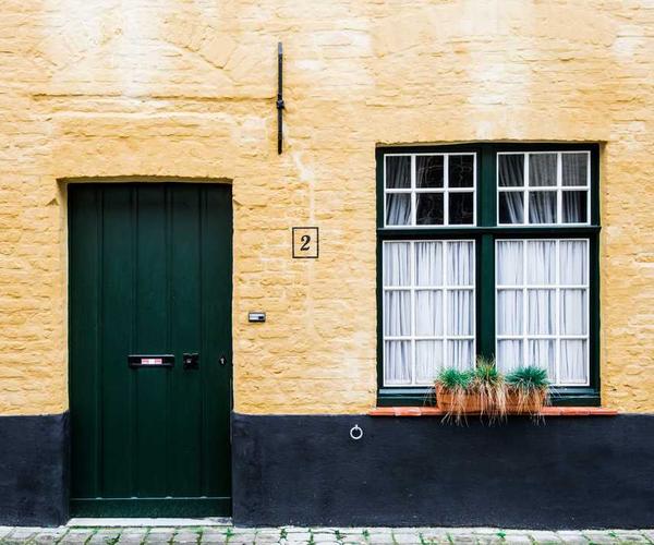 Gelbe Wand mit grüner Tür und Fenstern, typisches Wohnhaus für Immobilienberatung.