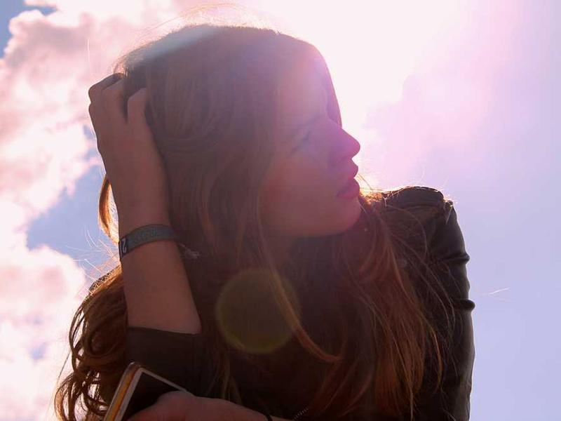 Nachdenkliche Person blickt in die Ferne vor hellen Wolken.