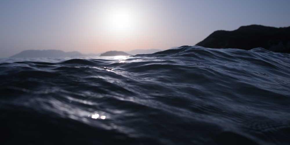 Ruhige Wasseroberfläche mit Sonnenlicht und Bergen im Hintergrund