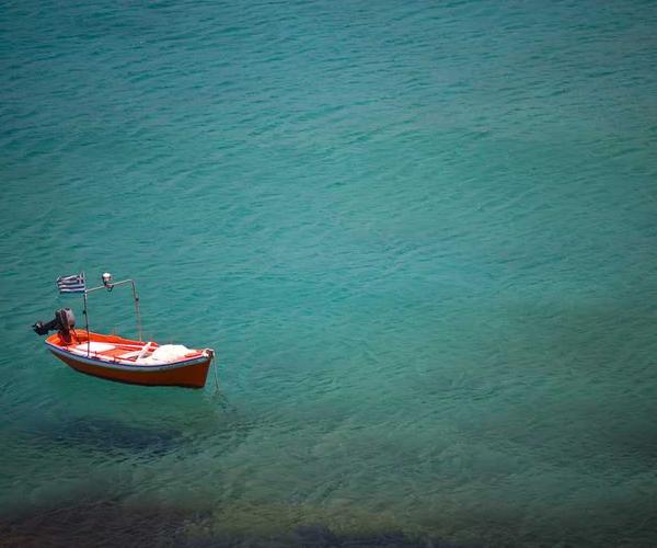 Kleines orangefarbenes Boot mit griechischer Flagge auf ruhigem Wasser.