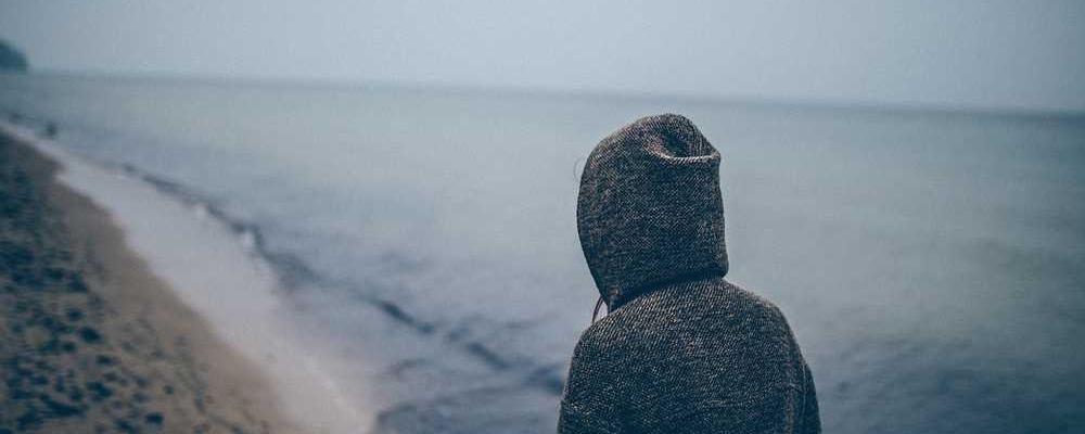 Person im Kapuzenpullover am Strand blickt nachdenklich auf das Wasser. RentPilot Blog.