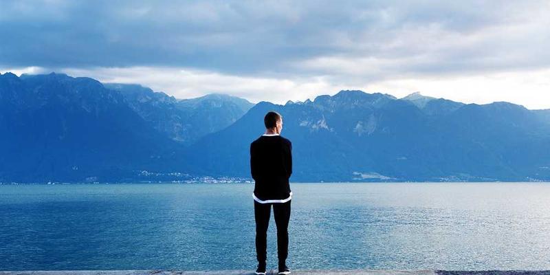 Person am Wasser blickt auf Berglandschaft für Blog über Immobilienverwaltung