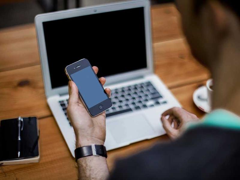 Person mit Smartphone vor Laptop zur digitalen Mietverwaltung RentPilot