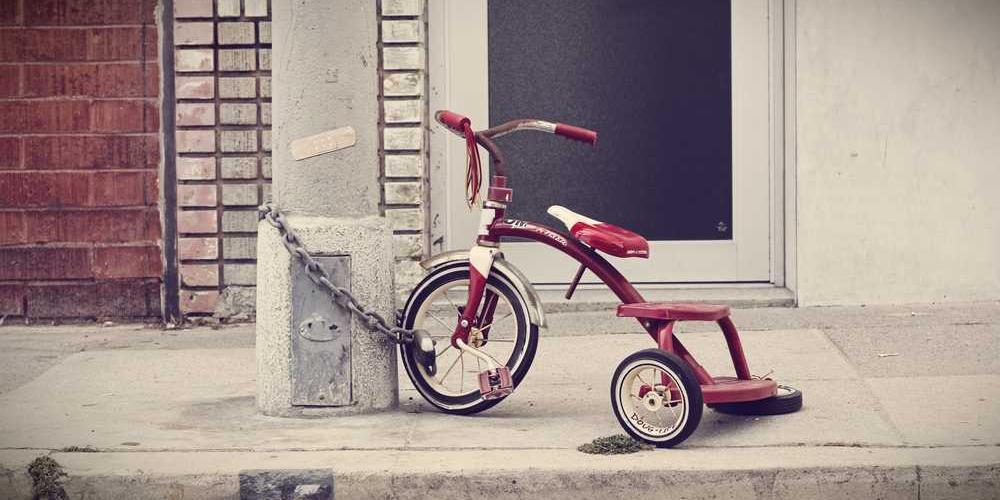 Rotes Dreirad an Laternenpfahl zeigt Nostalgie und Kindheit.