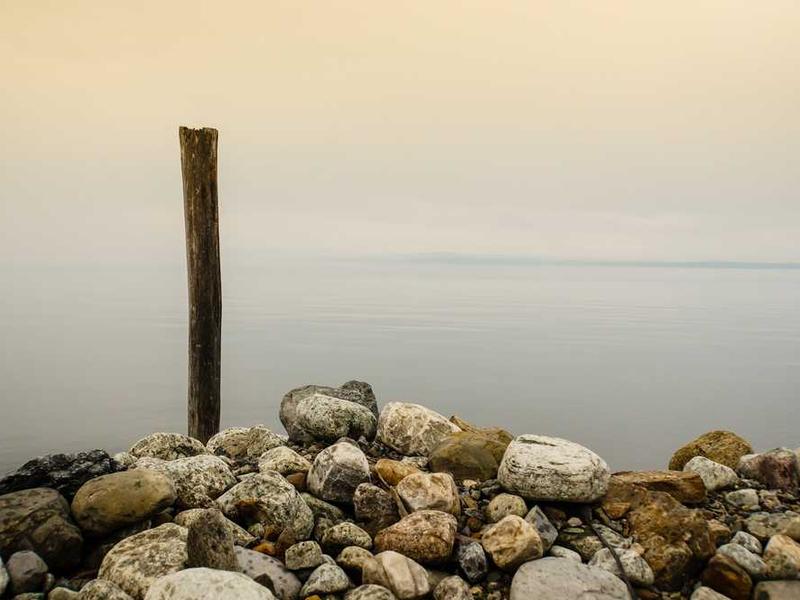 Ruhige Wasseroberfläche mit Steinen und Holzpfahl, natürlicher Hintergrund